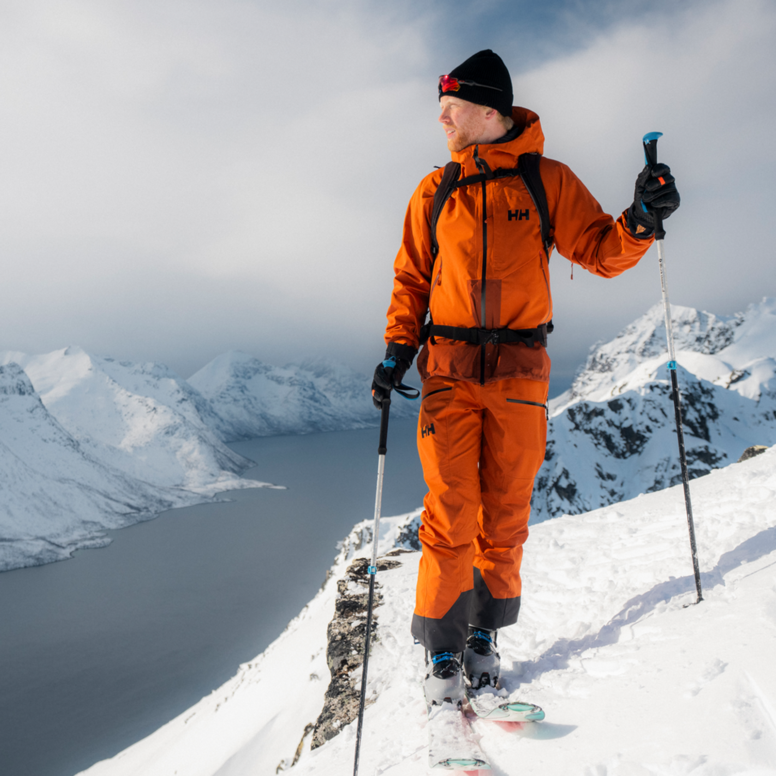 Helly Hansen Men's Verglas Backcountry Bib Shell Pants on skier on top of ridge overlooking inlet and mountains
