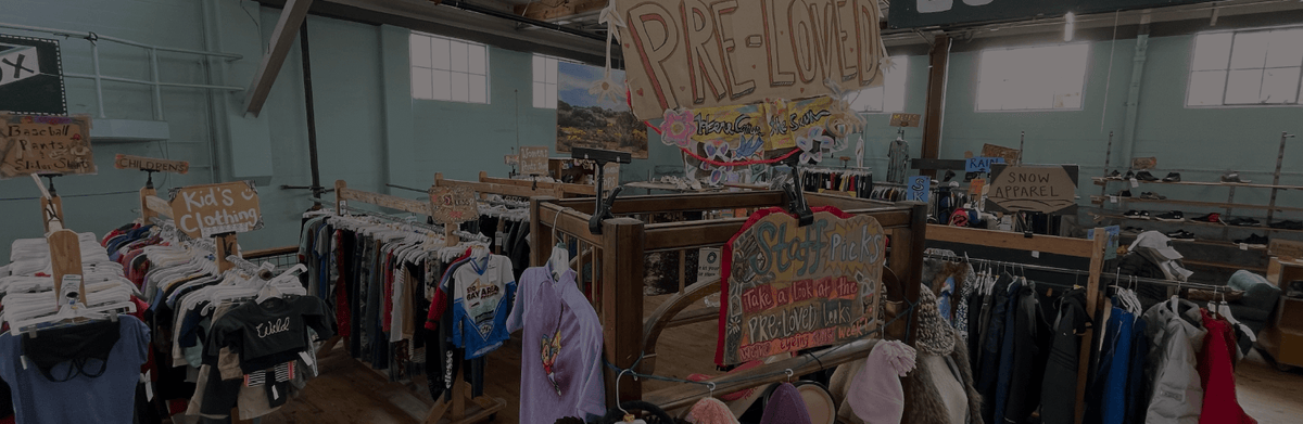 Used gear department filled with hand-drawn cardboard signs and colorful clothing on wooden racks.